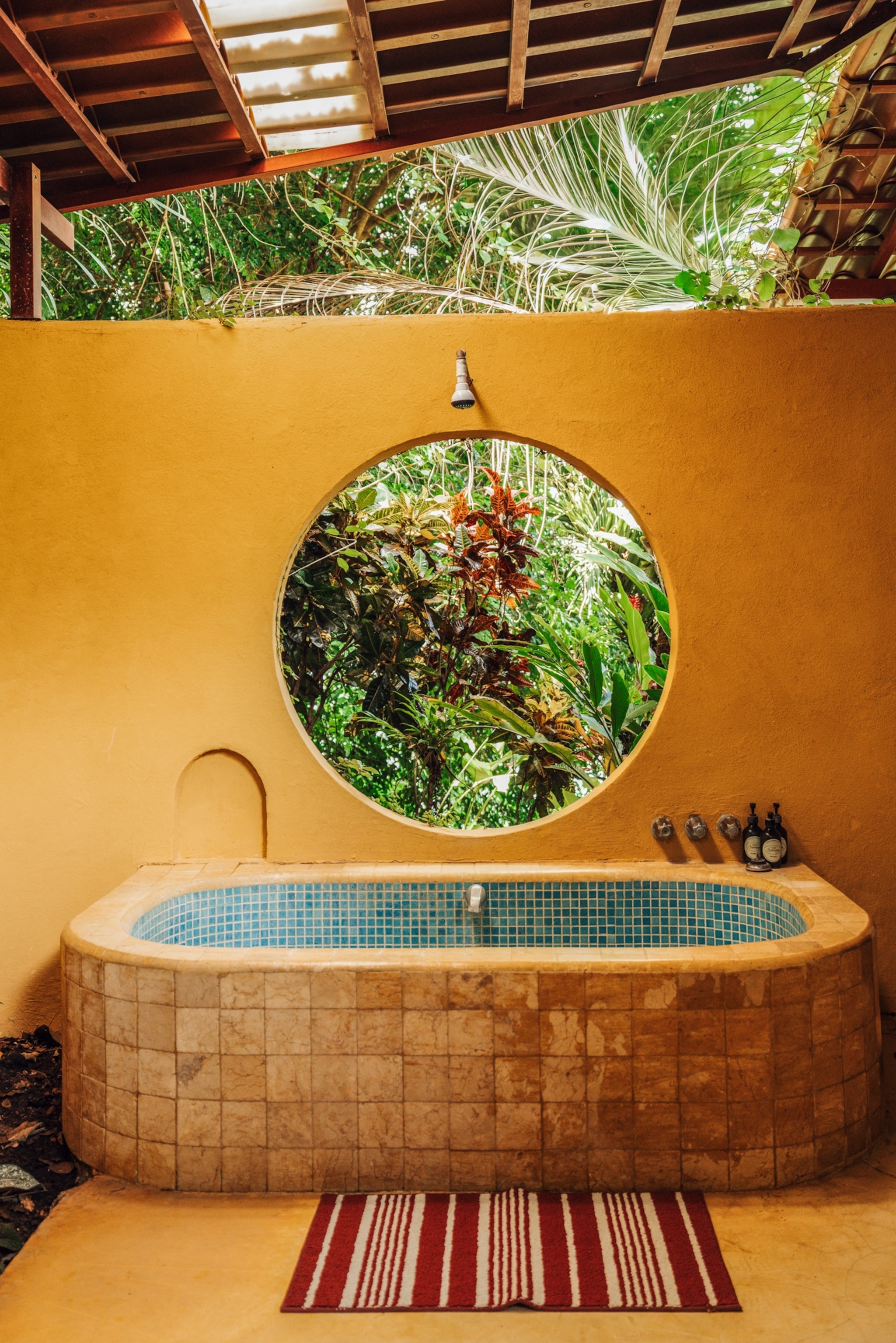 A circular window frames jungle views from the outdoor garden bathroom of Anamaya's Bali Cabina in Costa Rica's Nicoya Peninsula.