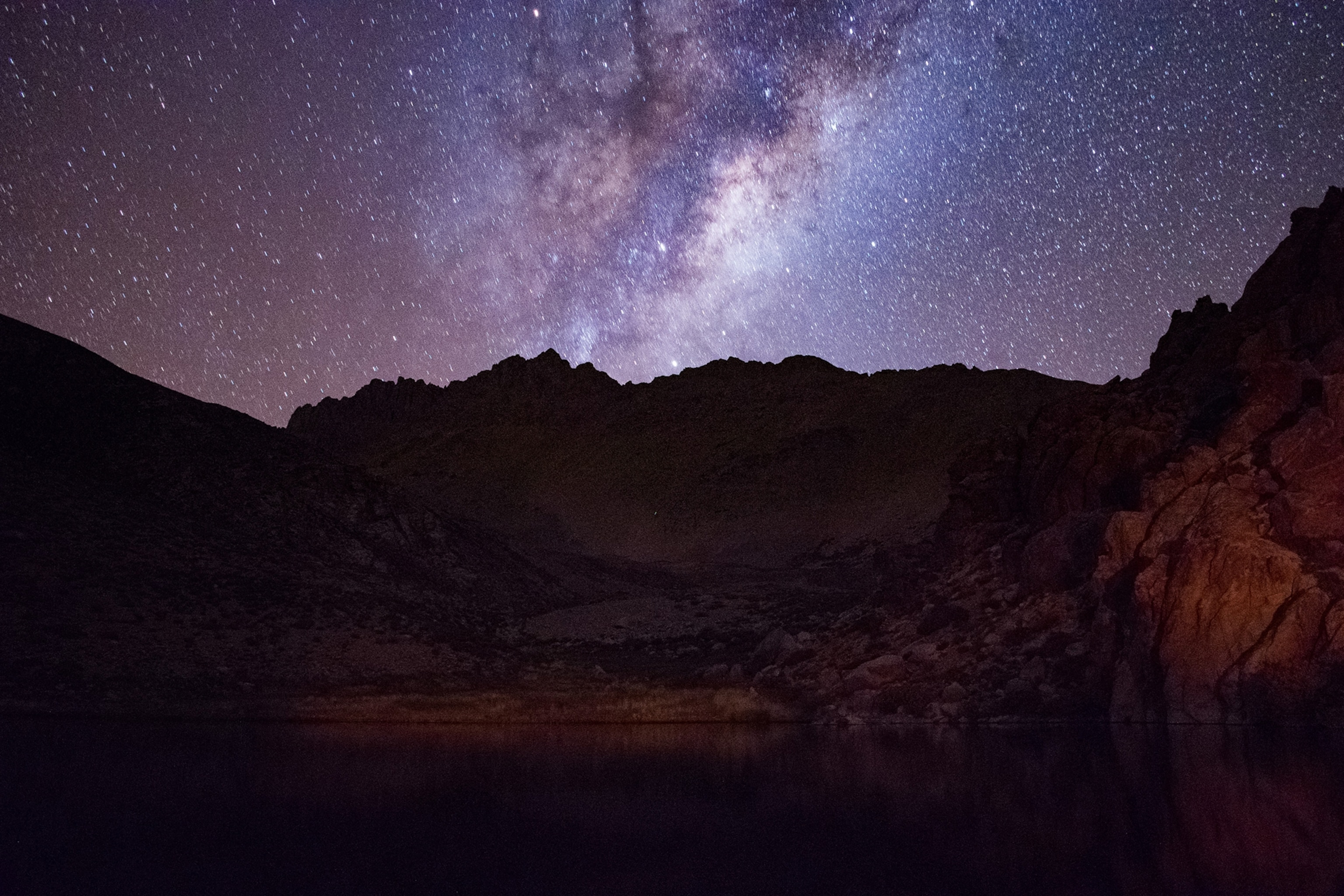 A night shot of a landscape with mountains as a skyline separating the dark earth and star-studded sky.