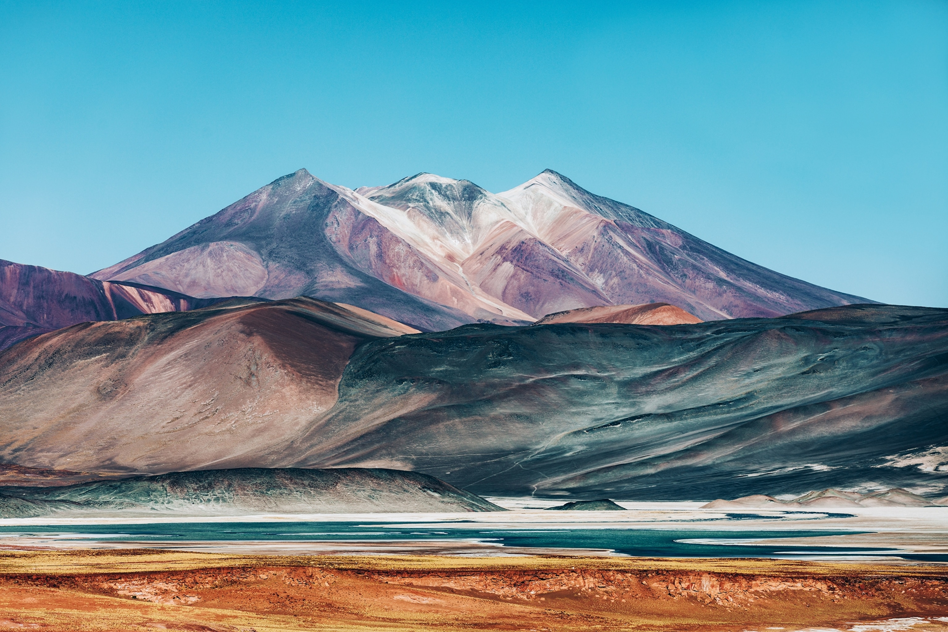 A wide landscape shot of a mineral-rich desert with a multi-coloured sand and a mountain in the background.