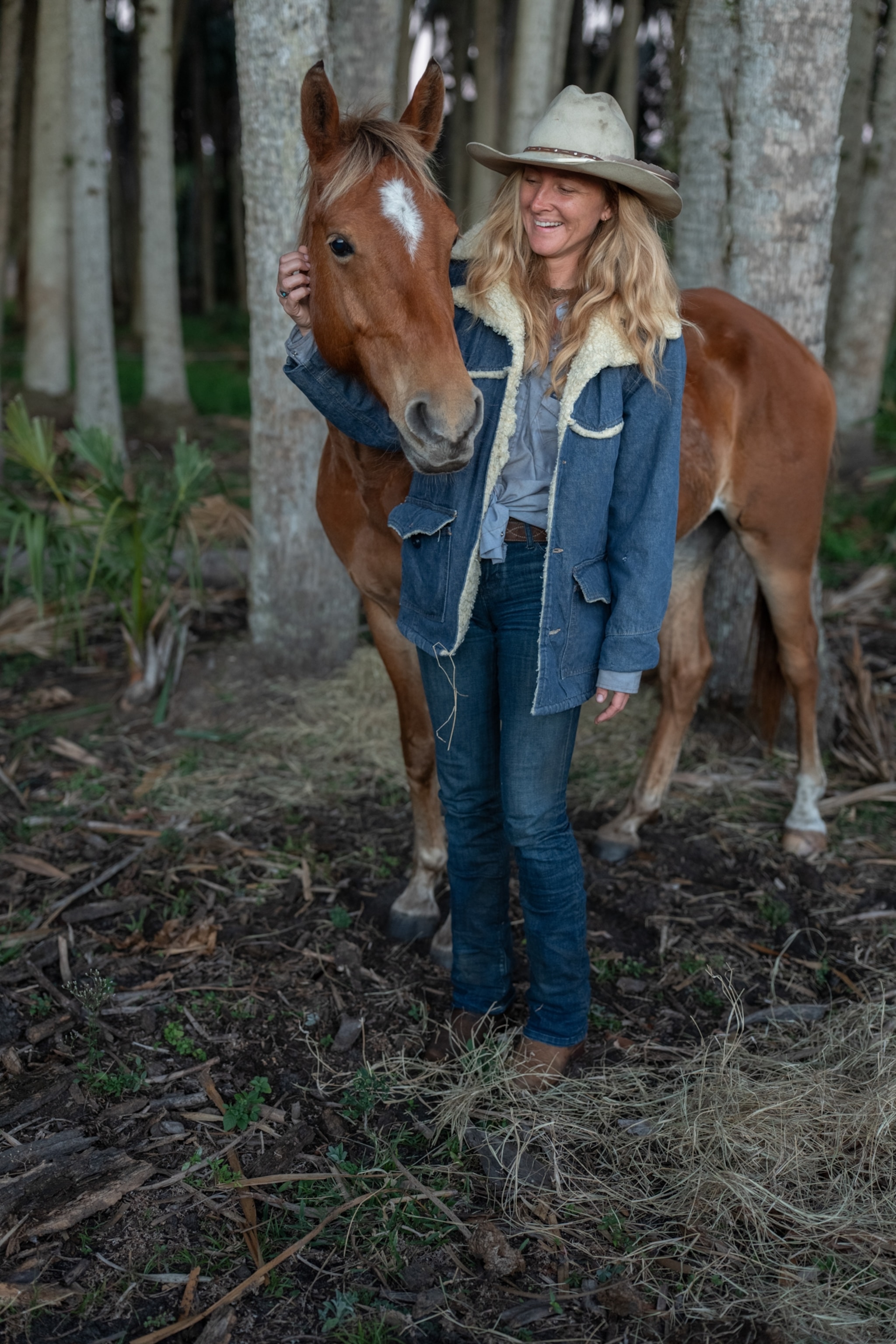 A woman in front of horse, and tress.