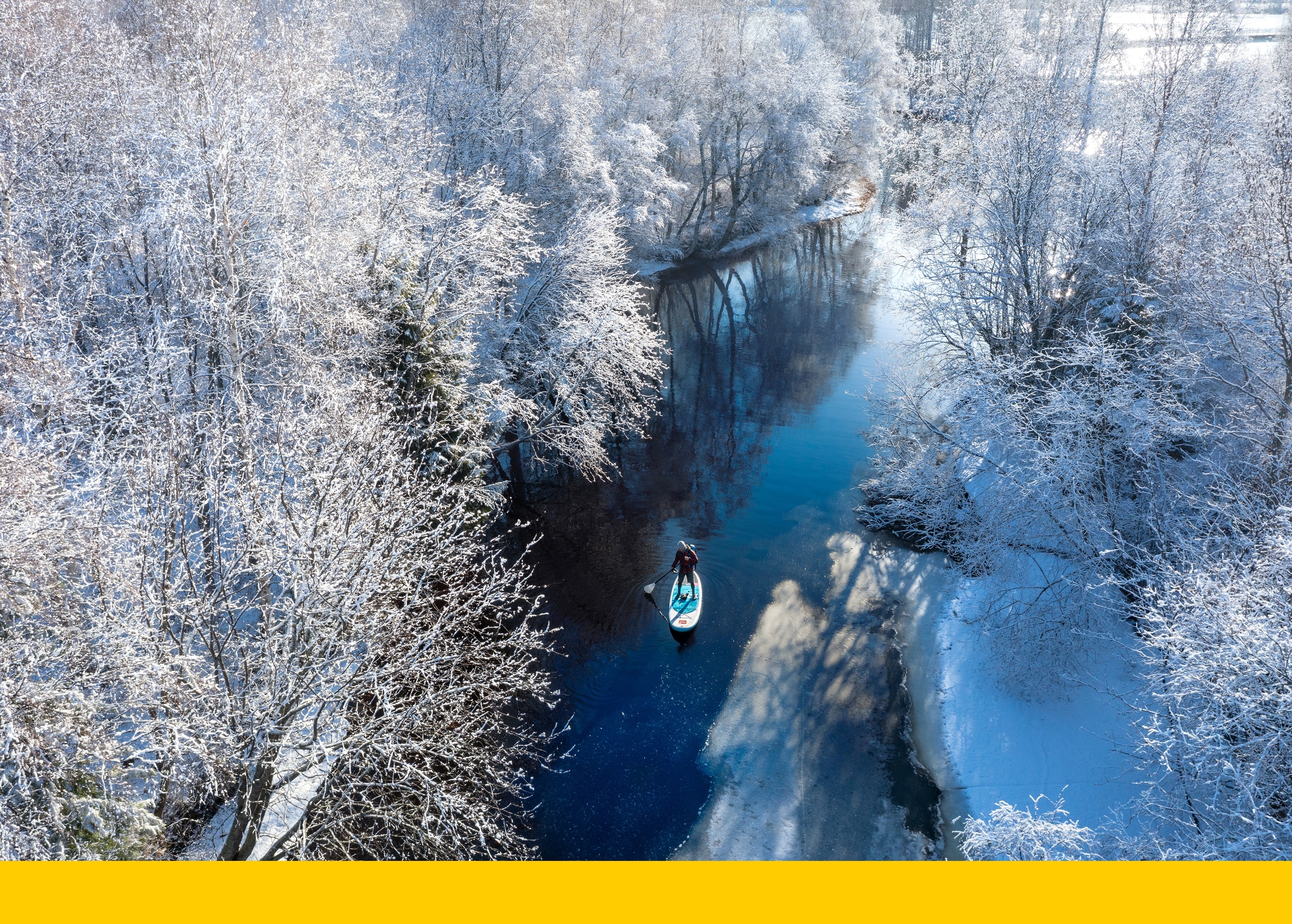 Paddle boarders make the picturesque journey through a winter wonderland.