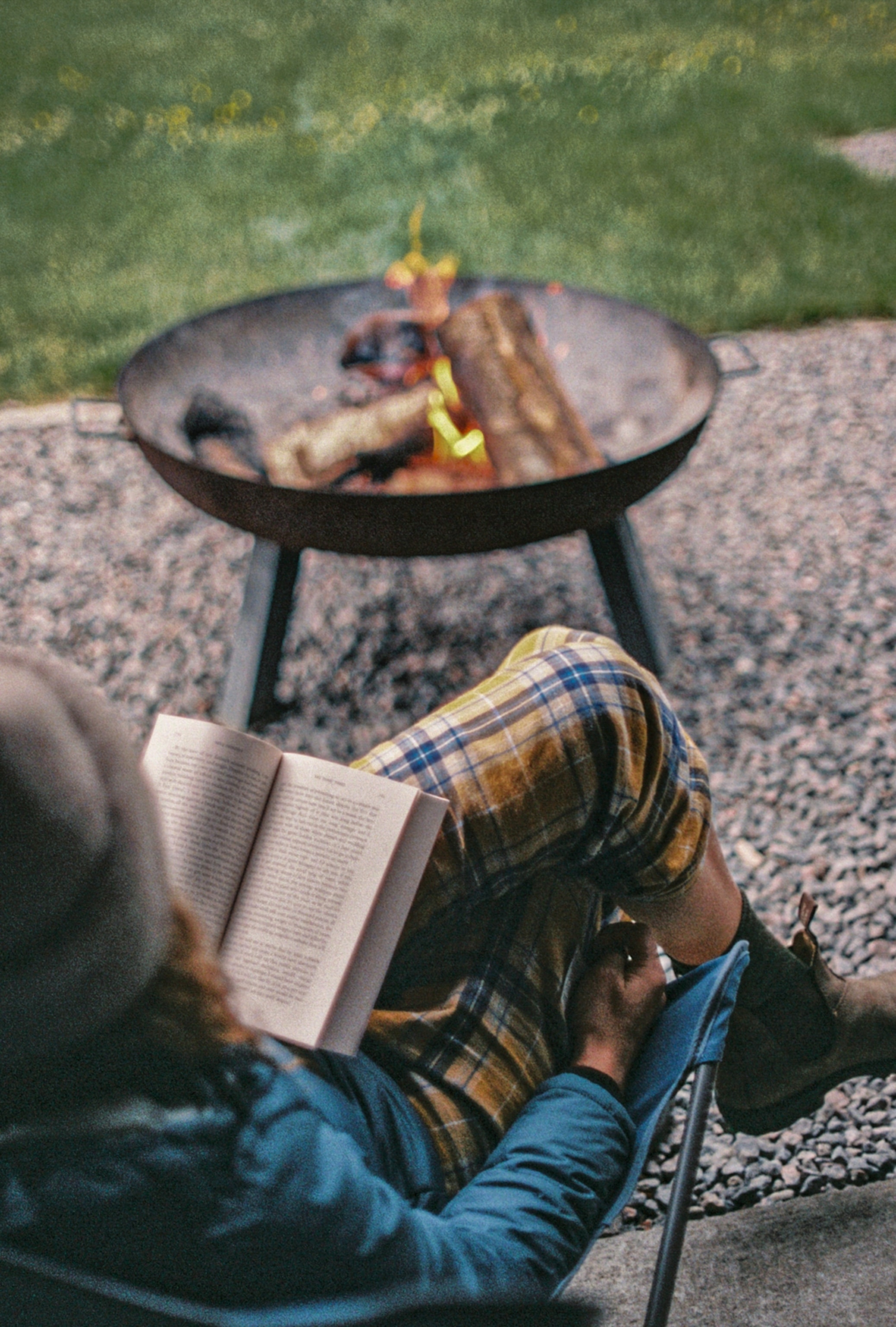 A woman sitting in a folding chair by the fire pit reading a book