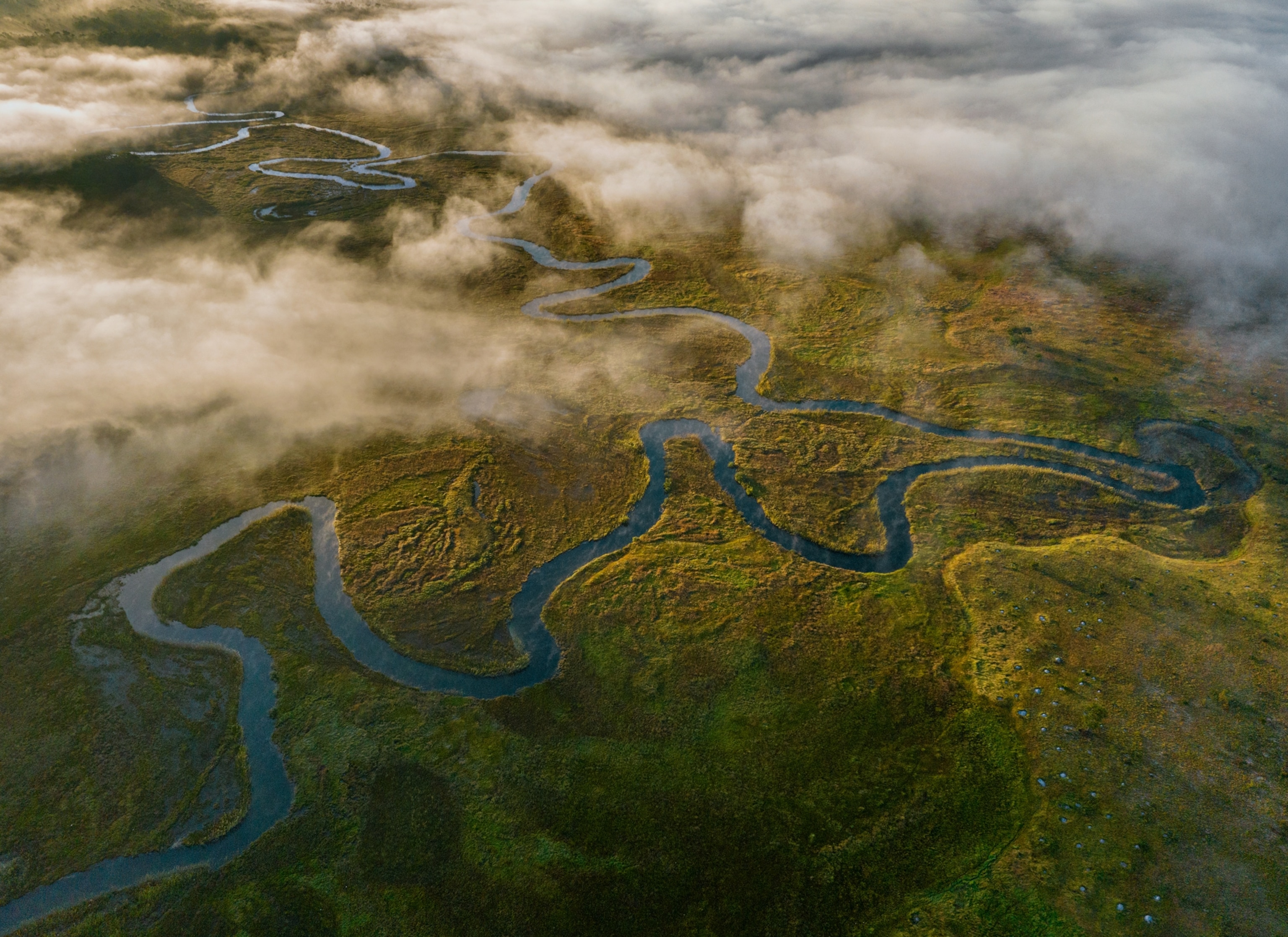Aerial view of winding river and swamp through clouds.