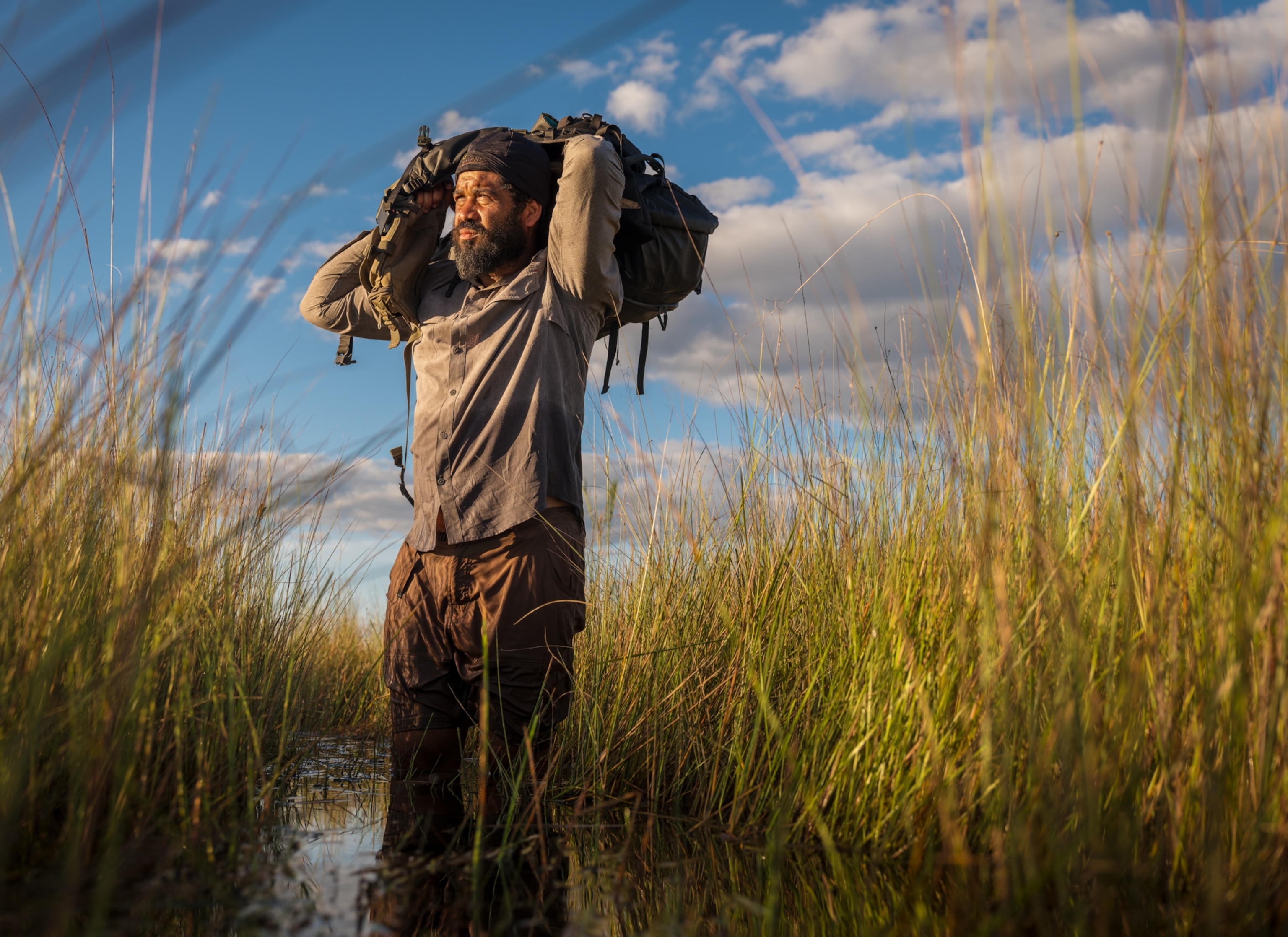 Man wades through the flooded grasses carrying backpack on is shoulders.
