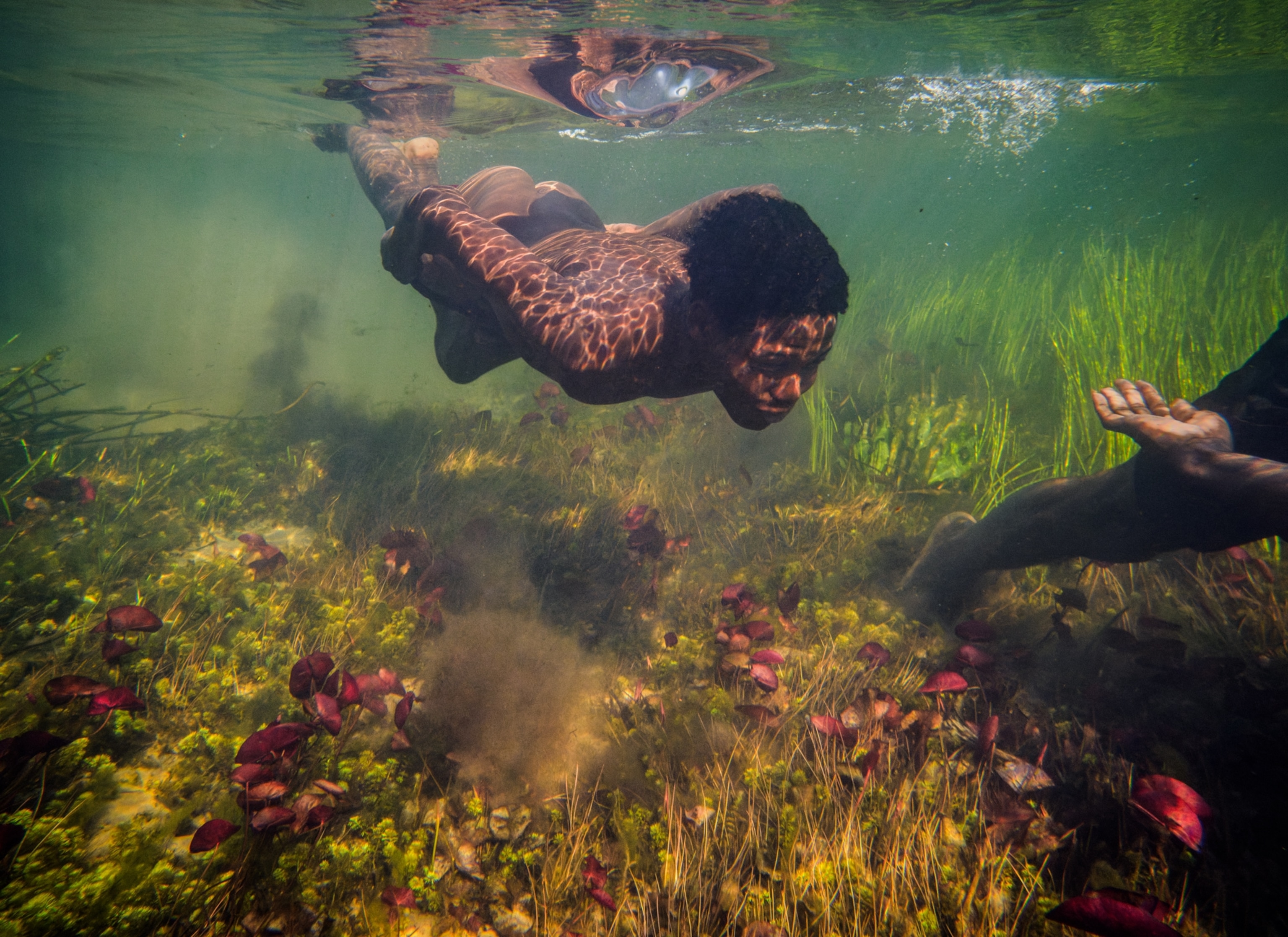 Underwater photo of young man swimming in the clear water and his reflection on water surface.