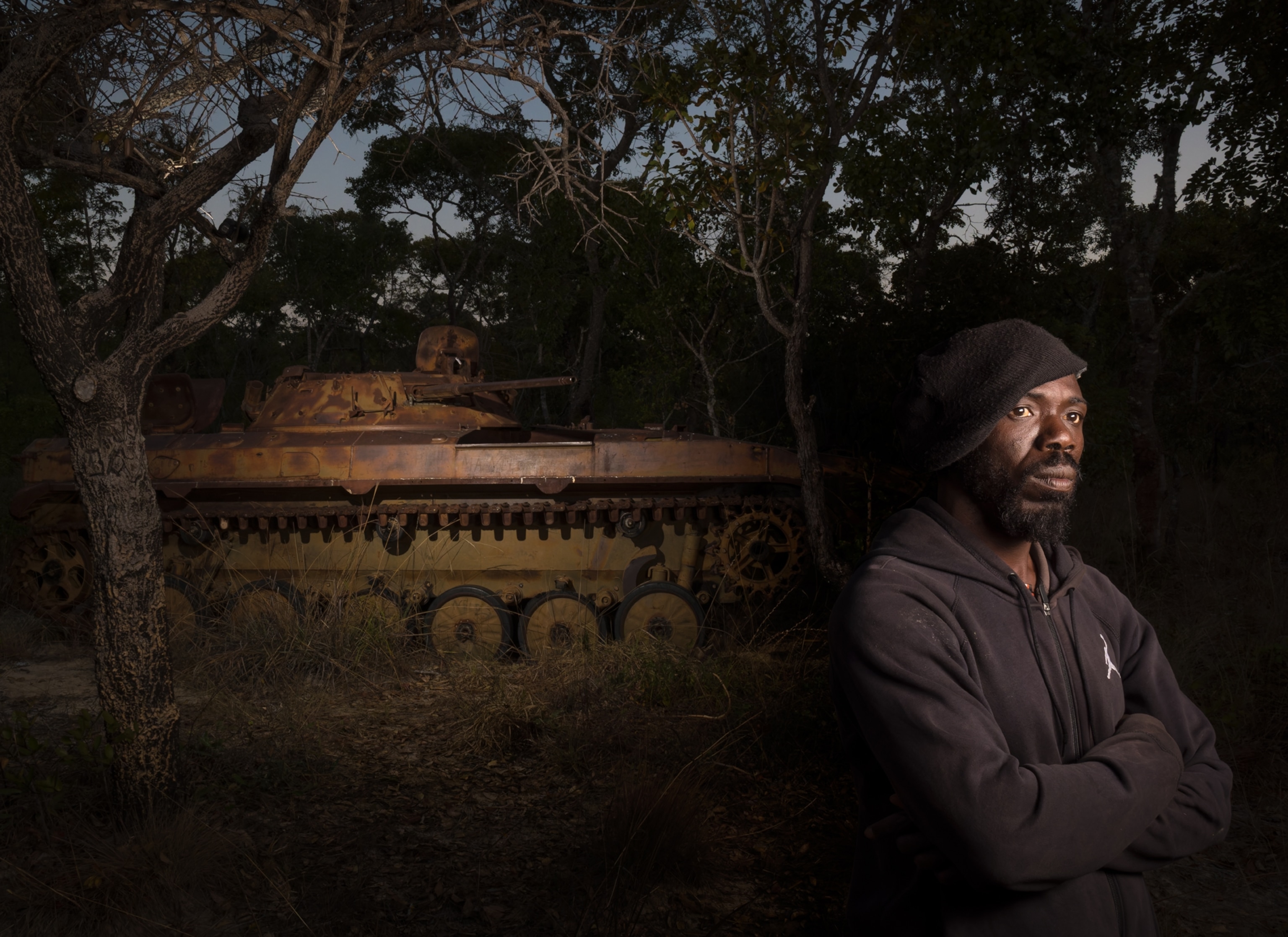 Man stands beside a rusting Soviet-era tank at dusk.