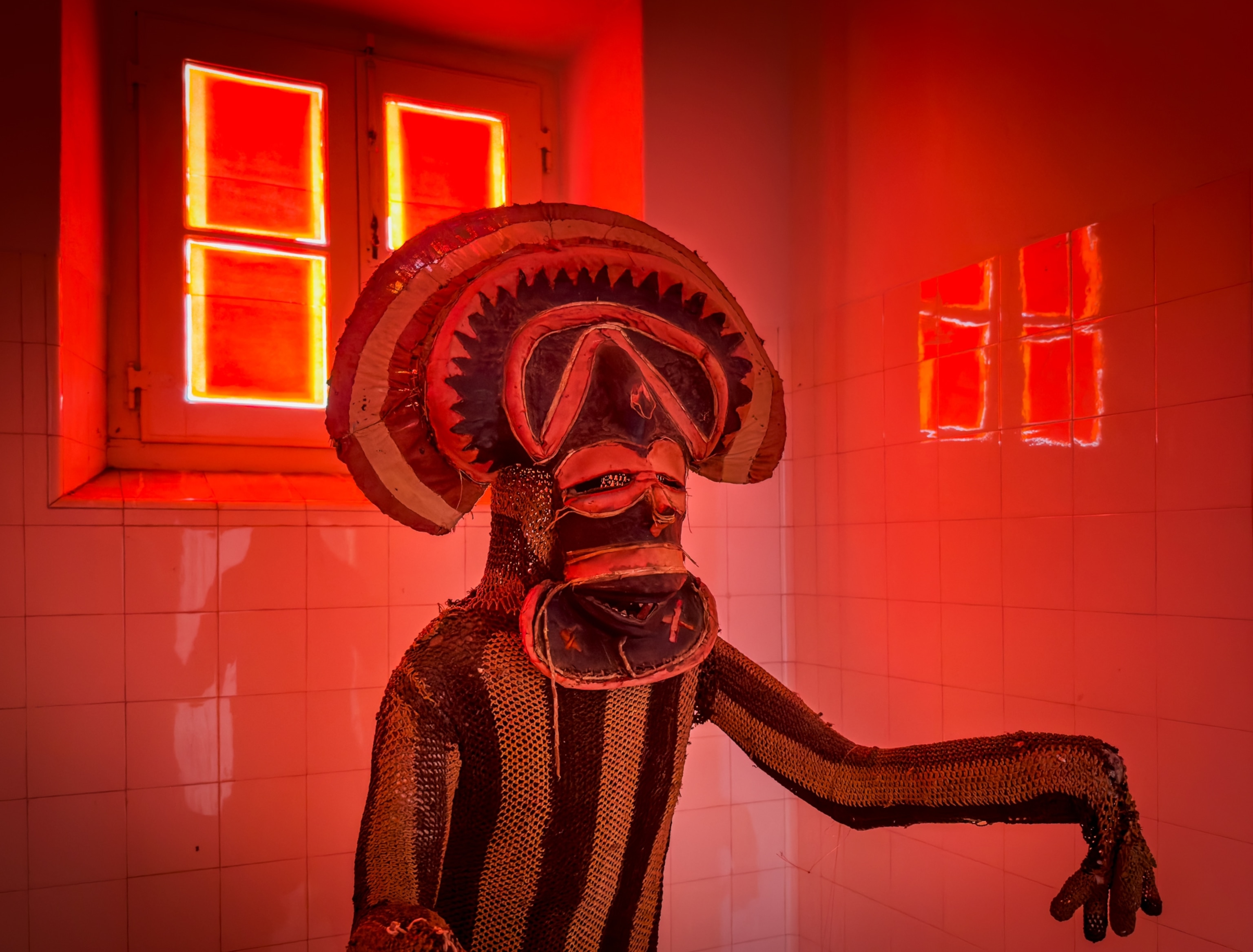 Museum display figure dressed in traditional costume and mask in red light.