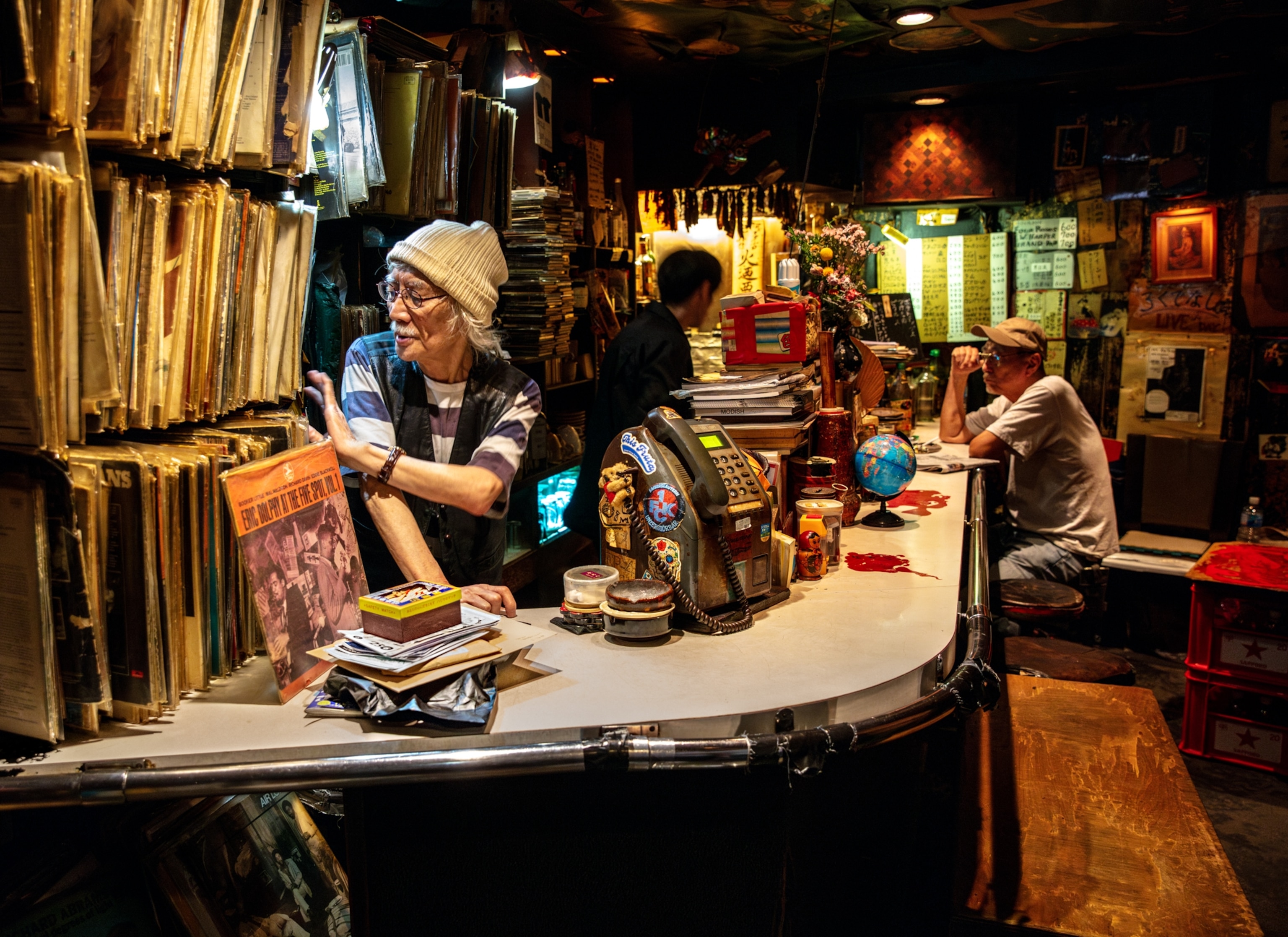 Elderly man in knitted hat looking through albums behind the store counter.