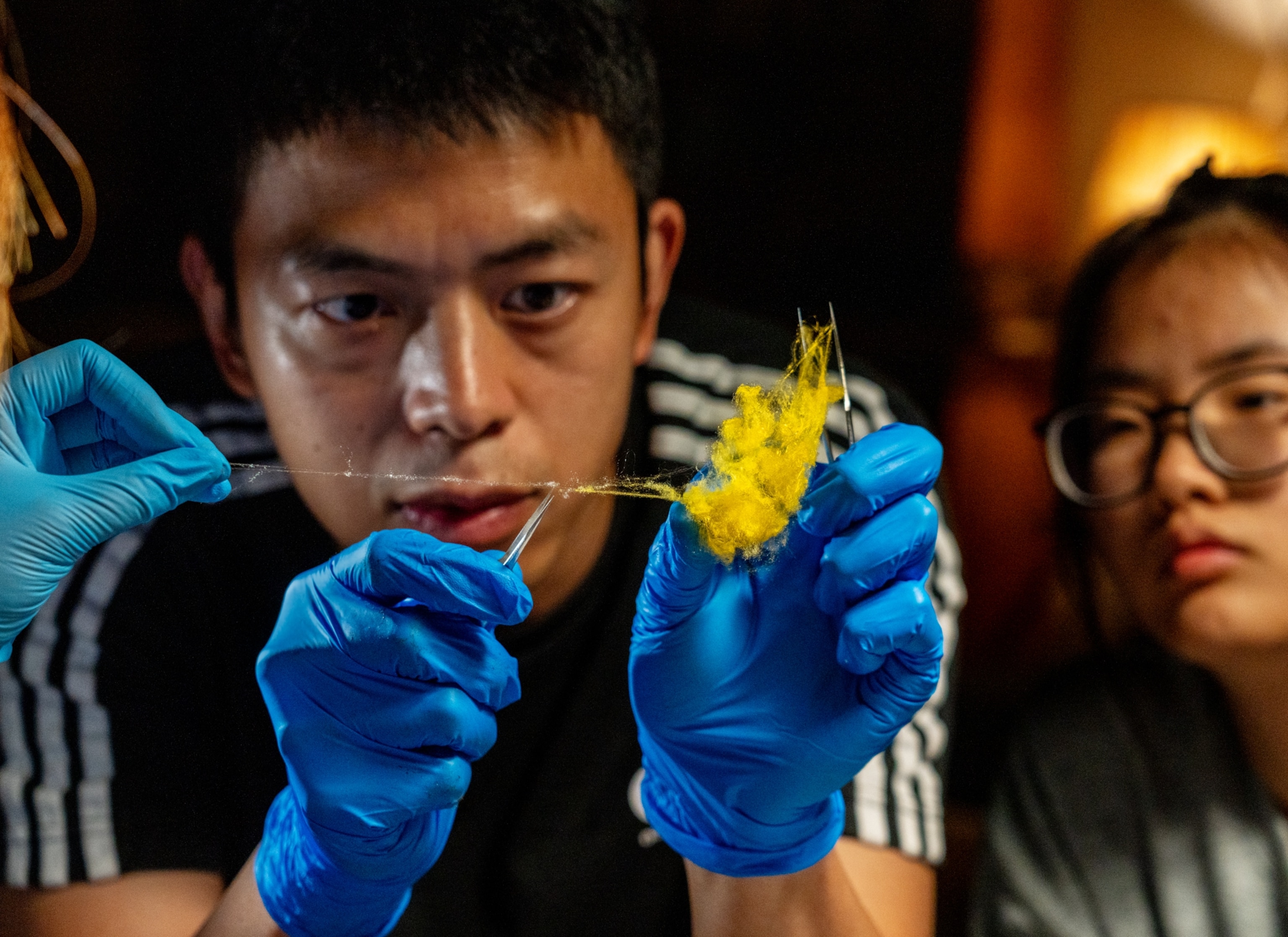 Young woman is watching young man manipulating with yellow thread.