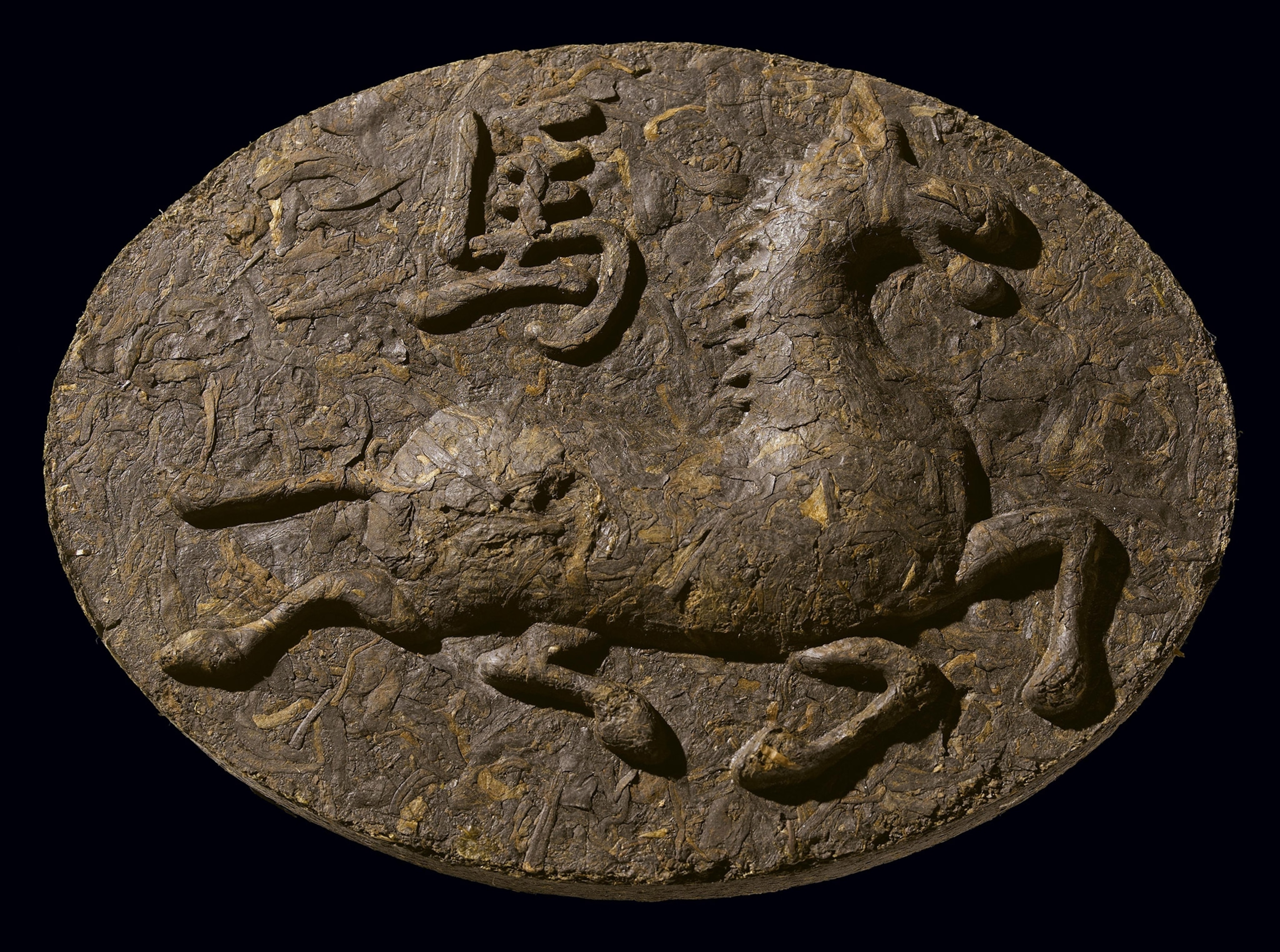A brown horizontal oval with rough texture with a horse figure and Chinese character in relief. 